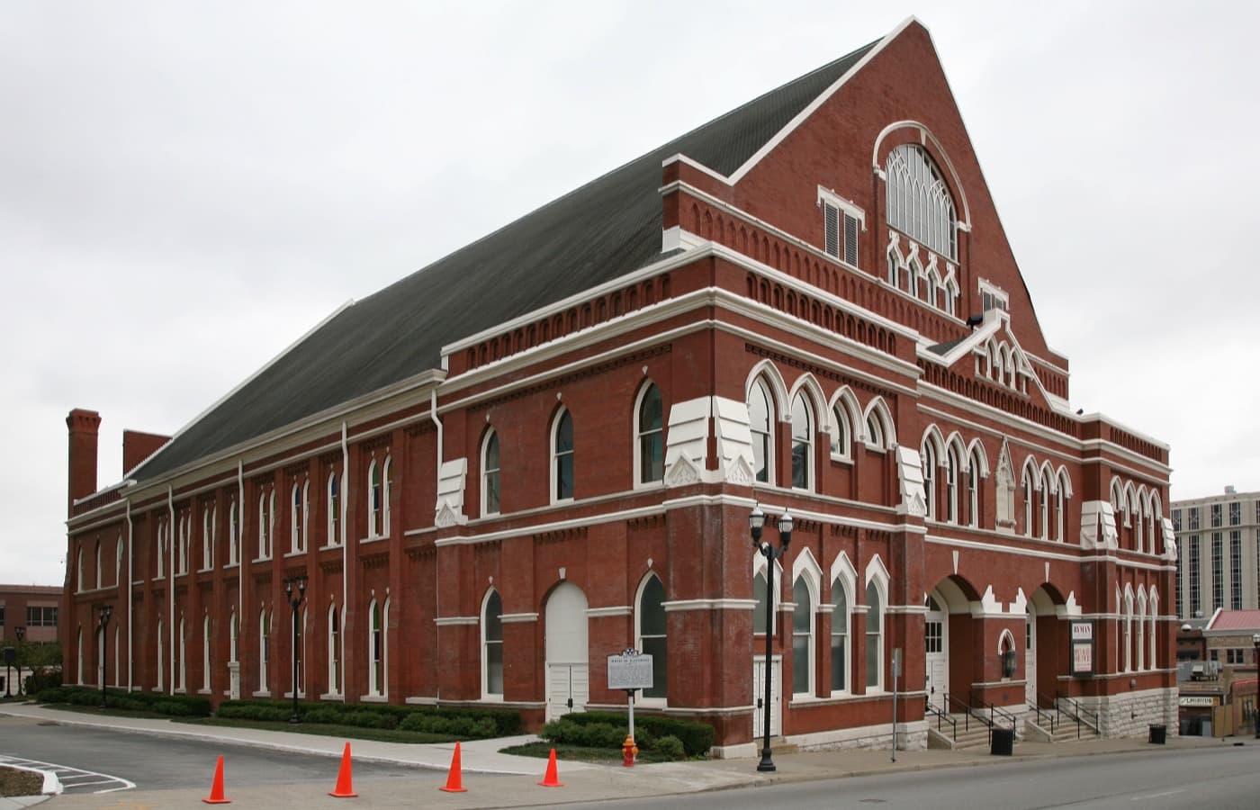 The red-brick Ryman Auditorium with tall arched Gothic windows and a steep gabled roof, on a street corner under an overcast sky